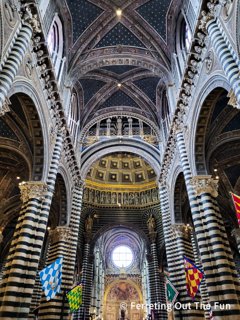 The dramatic black and white striped interior of the Siena Cathedral in Italy. The ceiling is a deep blue with gold stars.