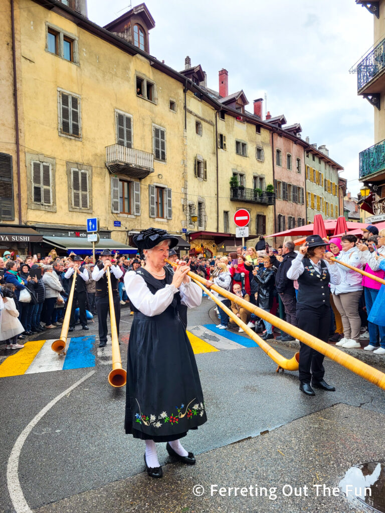 Musicians in traditional dress play alphorns in the Annecy Cow Parade